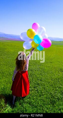 Happy girl in the meadows tuscan with colorful balloons, against the blue sky and green meadow. Tuscany, Italy Stock Photo