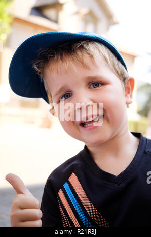 Outdoor portrait of 4 year old cool happy boy with blue baseball hat and black t-shirt giving thumbs up Stock Photo
