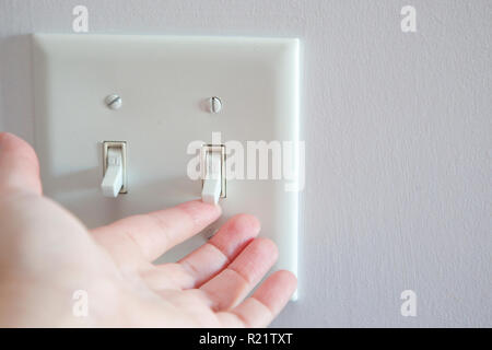 Hand about to turn a light switch from the off position to on Stock Photo