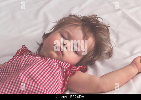 Baby girl sleeping on back with open arms and without pacifier in a bed with white sheets. Peaceful sleeping in a bright room. Pastel retro toned. Sof Stock Photo