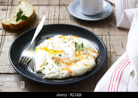 Cilbir, poached egg in yogurt with spiced butter and herbs, served with bread and a cup of coffee. Selective focus. Stock Photo