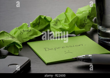 Depression. The word "depression" is written on green sticky note on wooden black table. Crumpled green sticky notes are scattered with texts written Stock Photo