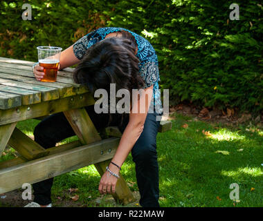 A drunk woman with a glass of beer in her hand, unconscious, leaning on a table Stock Photo
