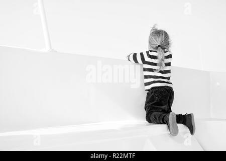 Small boy look from ship board, back view. Child on seat of boat on sunny blue sky. Kid with blond hair in navy clothes. Kids fashion and style. Summer vacation, travelling and wanderlust concept. Stock Photo