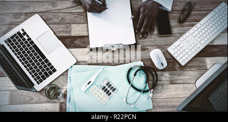 Doctor writing on clipboard at desk Stock Photo