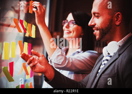 Coworkers sticking adhesive notes on glass Stock Photo