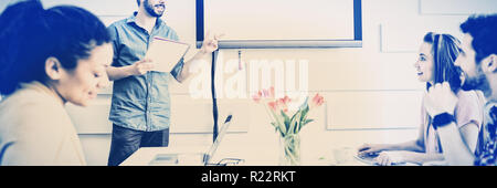 Happy executive giving presentation to colleagues in meeting room at creative office Stock Photo