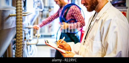 Maintenance workers examining brewery machine Stock Photo