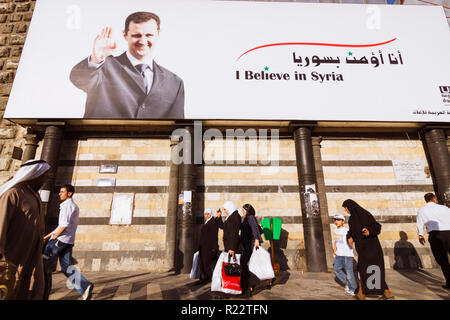 Damascus, Syria : People walk past a billboard of the president of Syria Bashar al-Assad reading I believe in Syria. Stock Photo