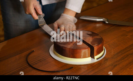 Prague mousse cake. Woman cuts off slice of cake with a kitchen knife. Mirror glaze glitters deliciously. Modern cooking. Cooking in a pastry shop. Stock Photo