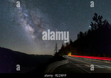 Under a night sky with Milky Way above, auto taillights streak through the scene and into a tunnel on Big Oak Flat Road in Yosemite National Park, CA. Stock Photo