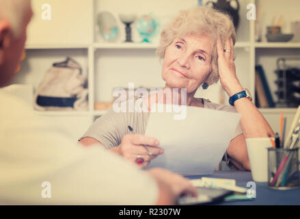 Upset senior woman sitting at home table discussing with husband their bills Stock Photo