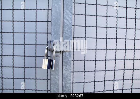 Padlock on a chainlink fence / Master key and old rusty chain with steel cage, close up / Closed lock with a chain on an old metal fence / Metallic, Stock Photo