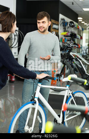 Young cheerful  smiling man seller demonstrating bicycle to woman client in store Stock Photo