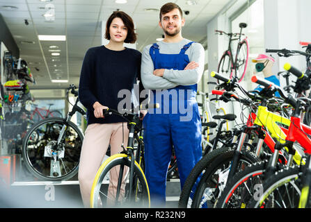 Cheerful  young woman and seller standing with bicycle in the store indoors Stock Photo