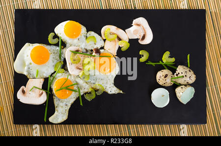 Fried quail eggs with mushrooms, chives and celery on wooden table Stock Photo