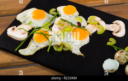 Fried quail eggs with mushrooms, chives and celery on wooden table Stock Photo