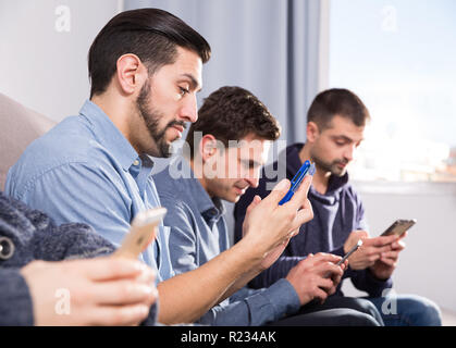 Male friends using mobile gadgets on sofa at home Stock Photo