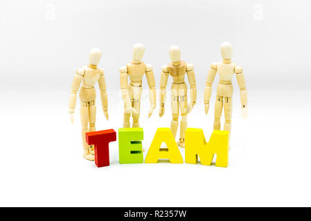 Wooden figures posing as business men behind the word TEAM, high key isolated on white. Team, unity and collaboration concept Stock Photo