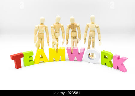 Wooden figures posing as business men behind the word TEAMWORK, isolated on white. Team, unity and collaboration concept Stock Photo