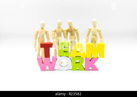 Wooden figures posing as business men behind the word TEAMWORK, isolated on white. Team, unity and collaboration concept Stock Photo