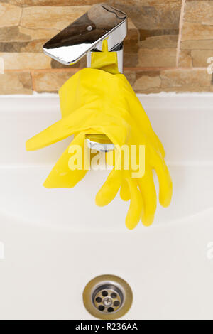 Yellow rubber hygienic gloves hanging on inox water tap Stock Photo