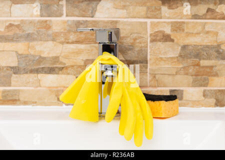Grey water tap with yellow rubber gloves hanging and orange sponge near Stock Photo
