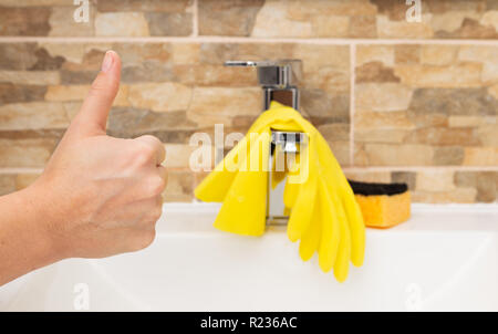 Thumb up gesture as approve concept in front of clean sink with yellow gloves and sponge Stock Photo