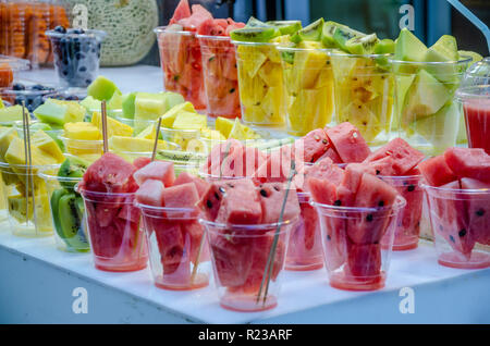 Plastic glasses of chopped fruit, watermelon, kiwi and pineapple ready to blend into a juice on display at a market street food stall. Stock Photo