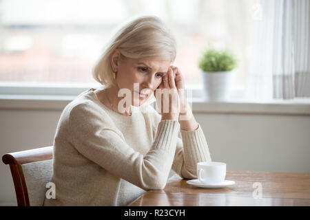 Worried senior woman sitting at table at home lost in thoughts, concerned aged female distracted from reality thinking about problems, sad elderly wif Stock Photo
