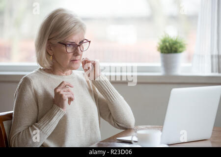 Surprised aged woman using laptop worried seeing error message on screen, concerned senior female get unexpected computer notification or warning, con Stock Photo