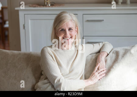 Portrait of smiling aged woman sit on cozy couch relaxing posing for picture, happy energetic senior female rest on comfortable sofa at home, elderly Stock Photo