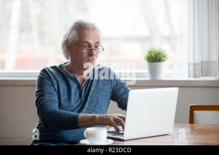 Surprised aged man stunned getting error or mistake message working at laptop, senior male using pc shocked by unexpected computer problem or virus at Stock Photo