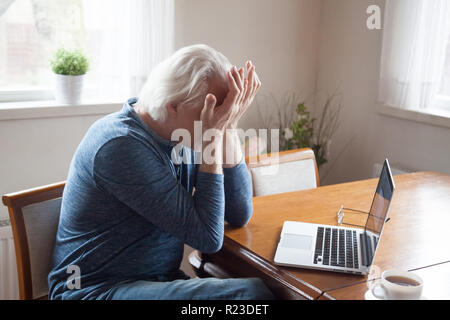 Tired aged man massaging eyes working too long at laptop, senior male feel exhausted suffer from headache after using computer, elderly having blurry Stock Photo