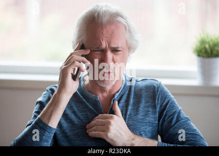 Angry aged man talk over cellphone arguing or having dispute with another person, determined senior male prove point of view involved in phone discuss Stock Photo