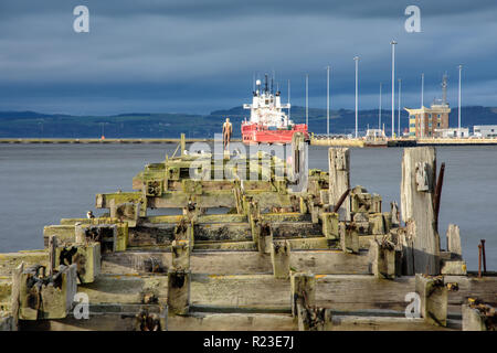 Edinburgh, Scotland, UK - November 3, 2018: Seabirds and an Antony Gormley statue stand on a derelict and abandoned pier in Leith Docks, with a docked Stock Photo