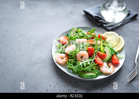 Avocado Shrimp Salad with Arugula and Tomatoes on grey stone background, copy space. Healthy diet green salad with Shrimps (prawns), avocado, cherry t Stock Photo