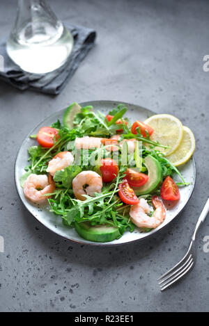 Avocado Shrimp Salad with Arugula and Tomatoes on grey stone background, close up. Healthy diet green salad with Shrimps (prawns), avocado, cherry tom Stock Photo