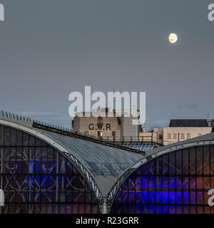 London, England, UK - September 21, 2018: An aeroplane crosses in front of the moon as it rises above London's Paddington Station. Stock Photo