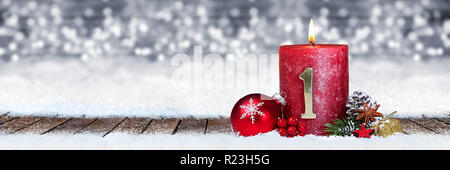 first sunday of advent red candle with golden metal number one on wooden planks in snow front of silver panorama bokeh background Stock Photo
