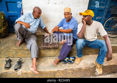 Three local African men are playing traditional board game Mancala. Stone Town, old colonial center of Zanzibar City, Unguja island, Tanzania. Stock Photo