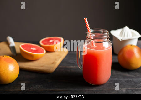 Freshly squeezed grapefruit juice in a jar with a handle. On a black wooden table are whole and sliced grapefruits and white manual juicer. Stock Photo