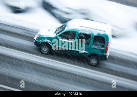 Blurry motion city traffic on a snowy day: A driving car in the street hit by the heavy snowfall