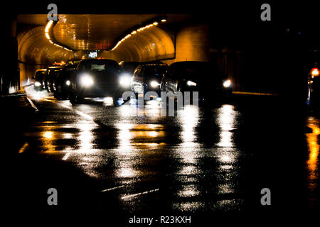 Night traffic on rainy city streets. Cars queued at tunnel exit waiting at intersection while driving vehicles moving past leaving color light trails Stock Photo