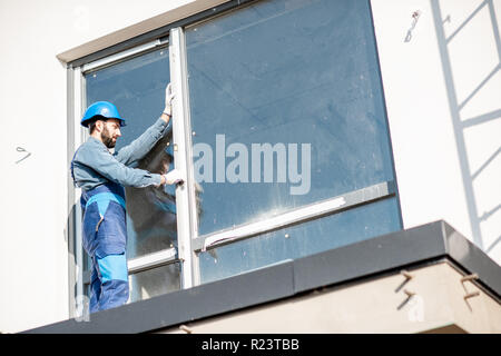 Workman in uniform mounting windows checking the vertical level standing on the balcony of the white building Stock Photo