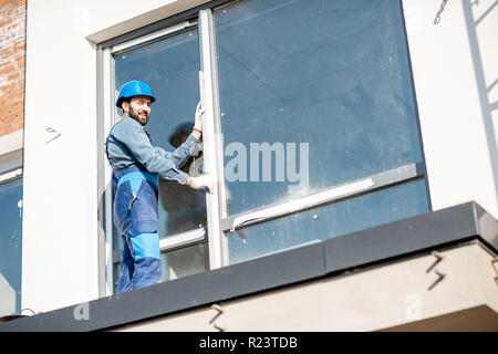 Workman in uniform mounting windows checking the vertical level standing on the balcony of the white building Stock Photo