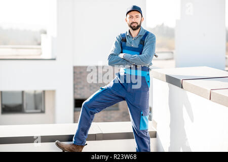 Portrait of a builder in uniform on the roof of a new white building outdoors Stock Photo