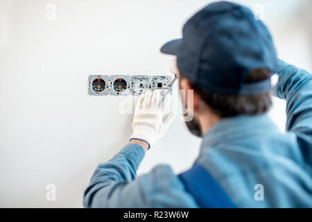 Electrician in uniform mounting electric sockets on the white wall indoors Stock Photo