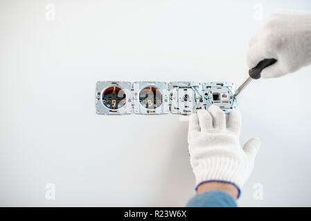 Close-up of an electrician mounting electric sockets on the white wall Stock Photo
