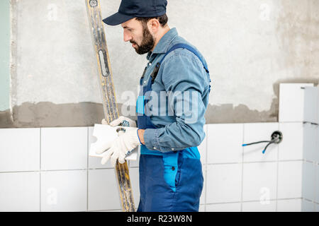 Workman in blue uniform installing white ceramic tiles at the bathroom Stock Photo